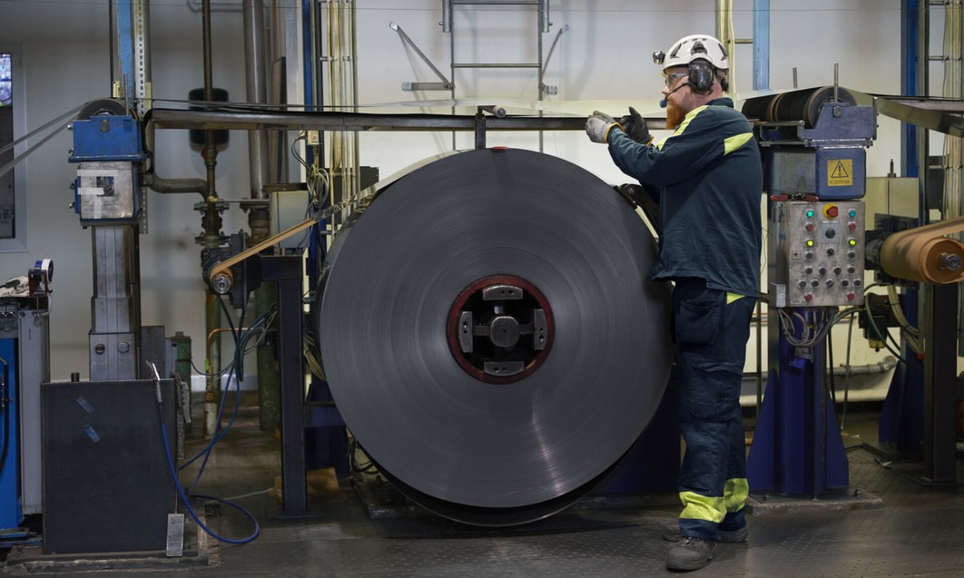 a person standing next to a large roll of metal