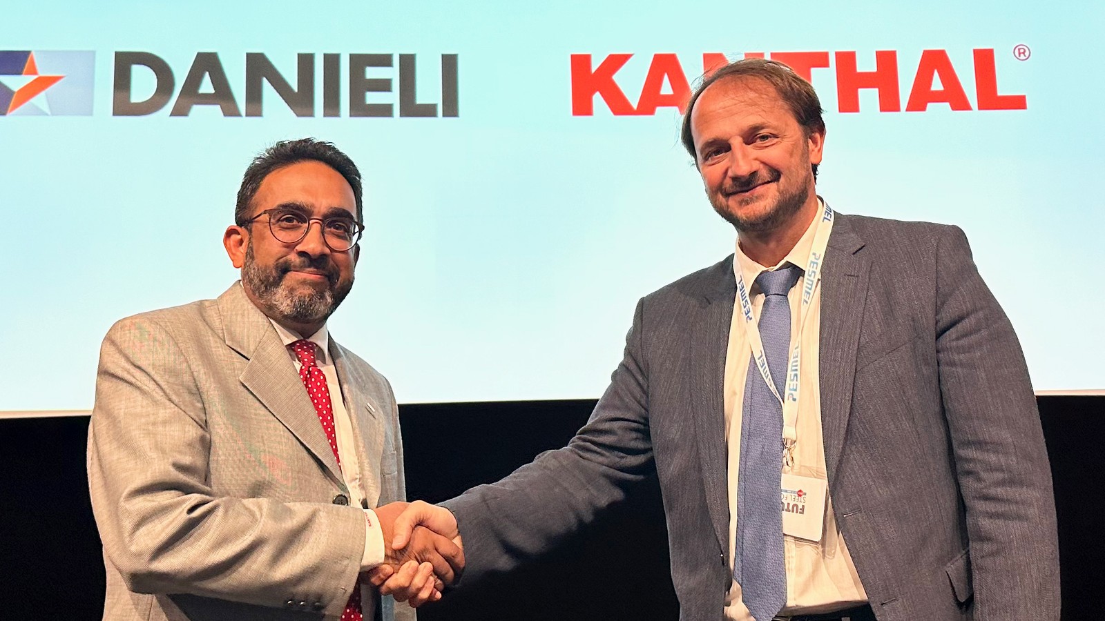 two men shaking hands in front of a screen