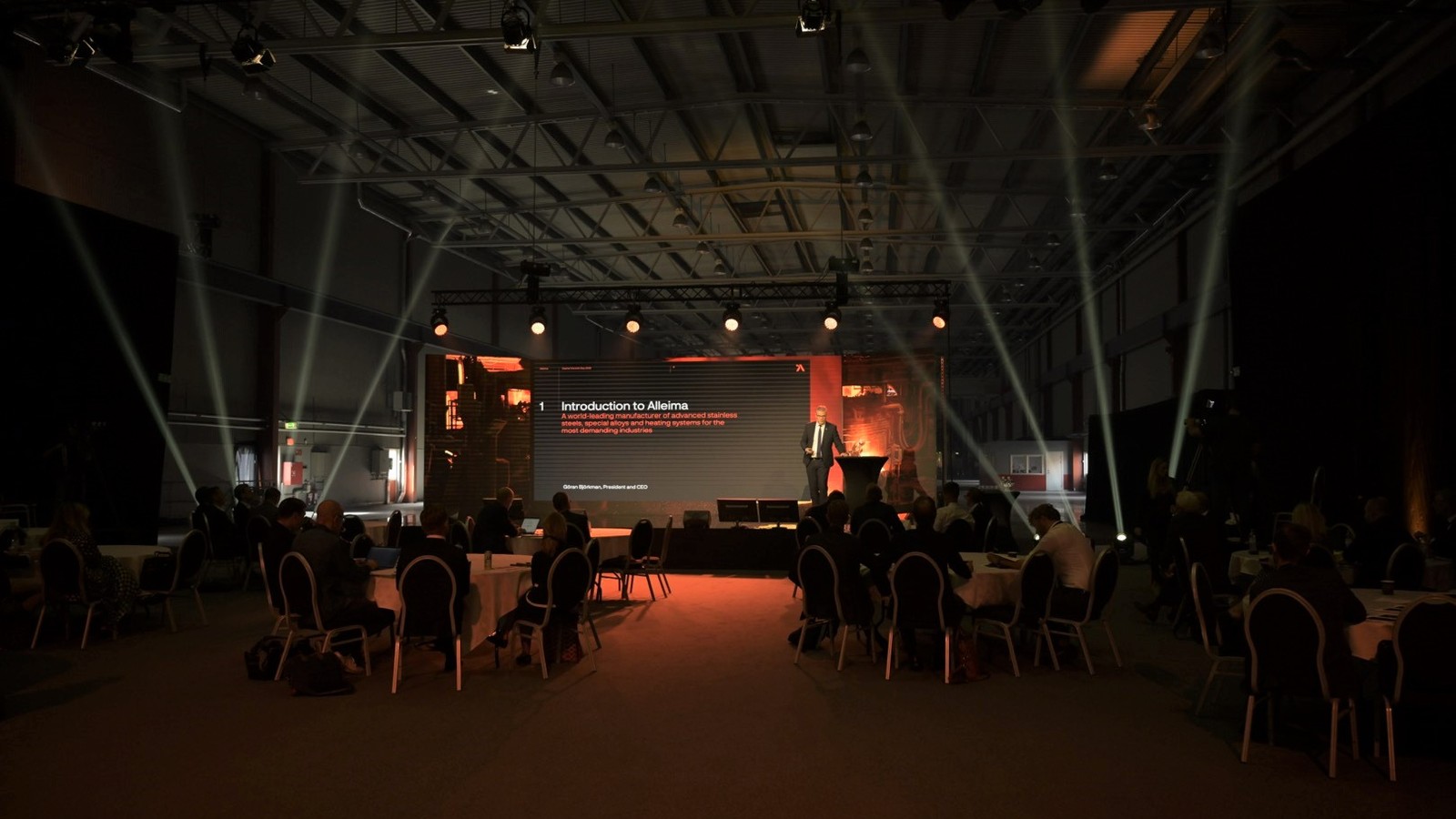 a group of people sitting in chairs in a room with a stage with lights