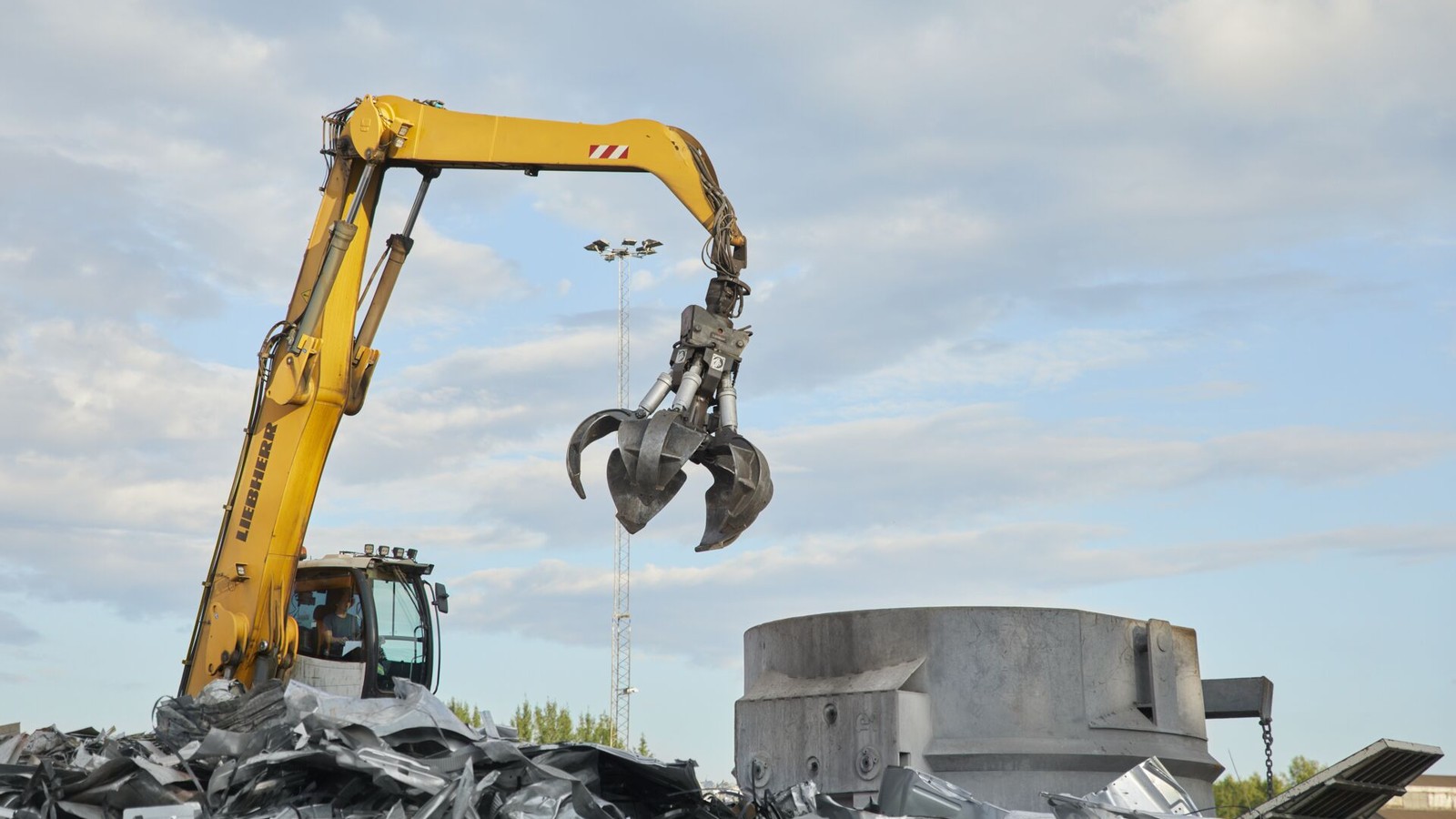 a yellow construction machine with a claw holding a metal object