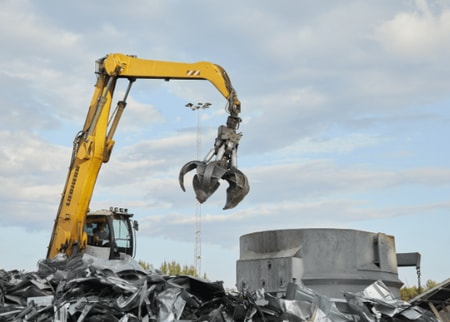 a yellow construction vehicle with a claw holding a metal object