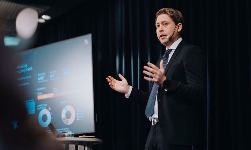 a person in a suit speaking in front of a screen